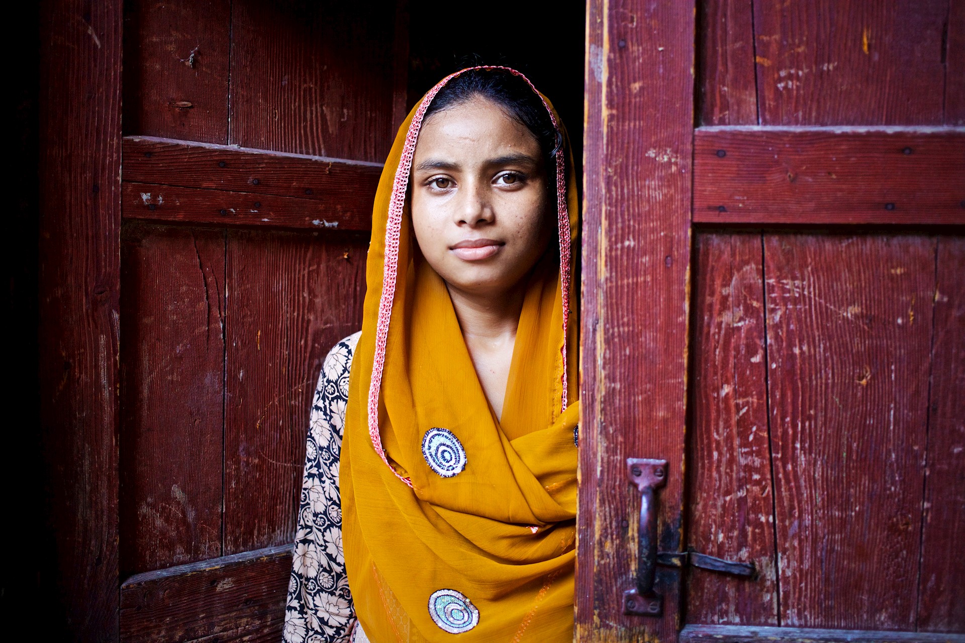 young girl looking to camera from behind a door