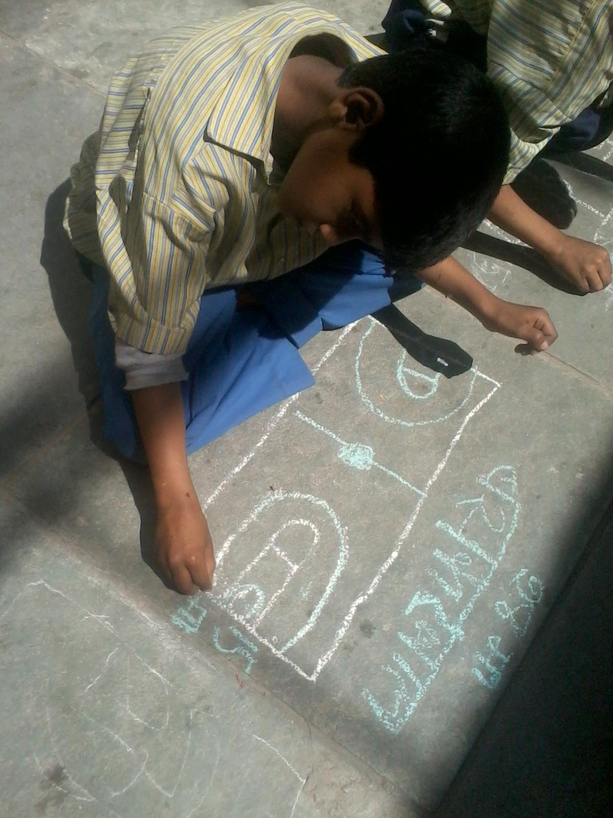 young boy writing with chalk on the ground 
