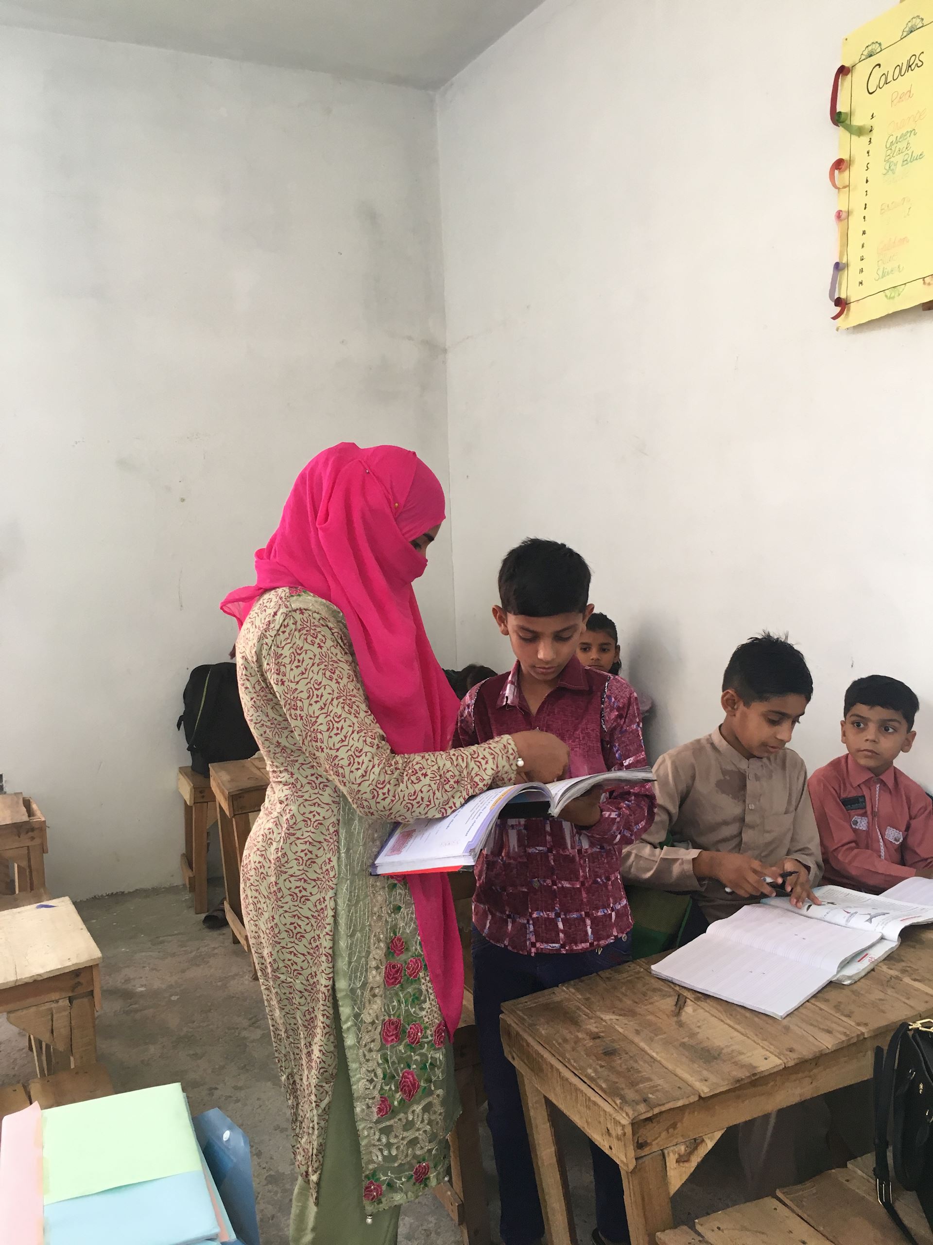 Teacher standing in class checking work of student, Pakistan
